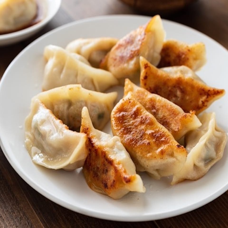 Plate of steamed and pan-fried dumplings on a wooden table, accompanied by rice and dipping sauce.