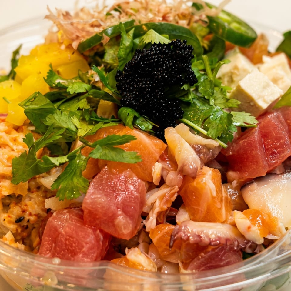 Colorful seafood poke bowl with tuna, salmon, mango, tofu, greens, crispy toppings, and black caviar in a clear dish.